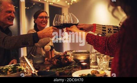 Dégustation de vin en famille au dîner de noël. Famille appréciant le dîner de noël ensemble à la maison, avec l'accent sur les mains et les verres à vin. Banque D'Images