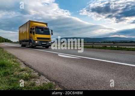 Circulation sur route avec camion de livraison de fret jaune en vitesse en bas de la route Banque D'Images