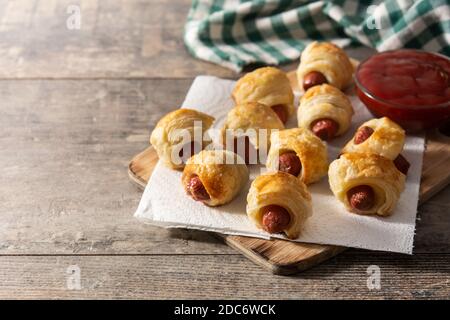 Cochons en couvertures. Mini saucisses enrobées de pâte feuilletée avec sauce ketchup sur une table en bois Banque D'Images