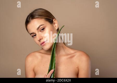 Soin de la peau, hydratant. Femme de beauté avec la peau parfaite tenant une feuille fraîche d'Aloe Vera. Femme avec maquillage naturel et portrait sain de peau. Banque D'Images