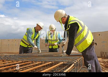 Trois ouvriers de construction assemblent une cage de renforcement en acier pour Béton insitu sur un grand chantier de construction de Londres Banque D'Images