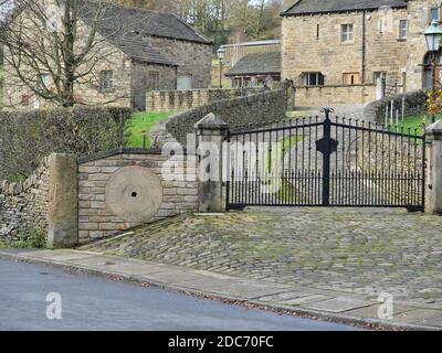 Allée pavée en bord de route, cercle de pierre fixé dans le mur de pierre inférieur Hagg Farm sculptée autour de lui deux portes en métal noir maisons en arrière-plan Banque D'Images