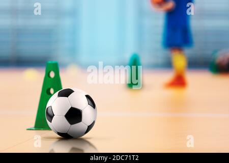 Football en salle - terrain d'entraînement de futsal. Ballon de football et cônes d'entraînement. Les enfants s'entraîner dans un arrière-plan flou Banque D'Images