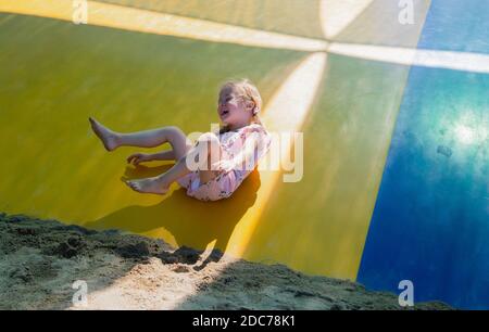 Petite fille blonde jouant dans le parc sautant sur un trampoline Banque D'Images