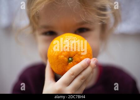 Petite fille blonde se cachant derrière un orange / un kaki Banque D'Images