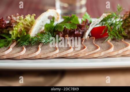 Délicieux plat de restaurant de langue de bœuf finement tranchée avec des herbes sur une grande assiette blanche avec une attention sélective. Banque D'Images