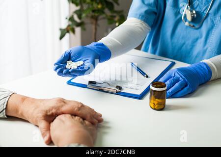 NHS GP UK médecin portant des gants de protection bleus en latex une poignée de pilules blanches, la donnant à la femme âgée patient senior, remède et guérison Banque D'Images