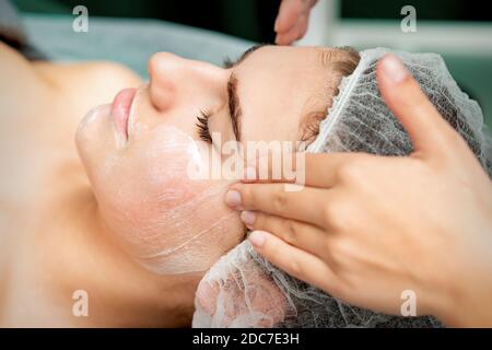 Jeune femme recevant un massage du visage avec les yeux fermés par une esthéticienne dans le salon de beauté Banque D'Images