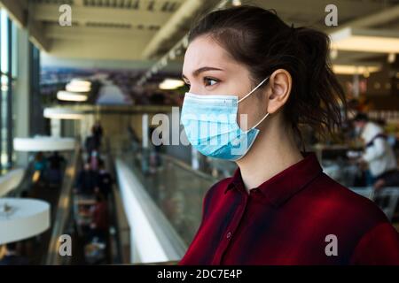 Belle jeune femme caucasienne, assez inquiète, portant un masque chirurgical protecteur, debout dans un centre commercial ou un supermarché, stressée et inquiète Banque D'Images