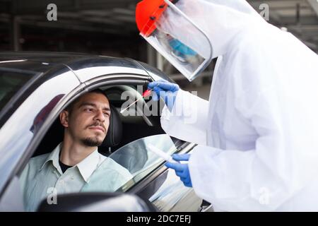 COVID-19 détection RT-PCR drive-in, diagnostic de point de contrôle de voiture, travailleur médical exécutant un écouvillon nasal prélèvement d'échantillons sur un jeune conducteur mâle jusqu'à Banque D'Images