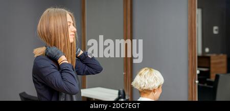 Le coiffeur féminin met un tablier noir avant de couper le client cheveux Banque D'Images