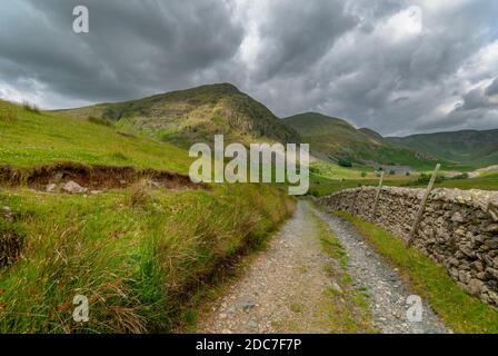 Une ancienne ferme avec un long mur de pierre sèche menant à des montagnes et des pâturages dans le district de cumbria lac. Banque D'Images