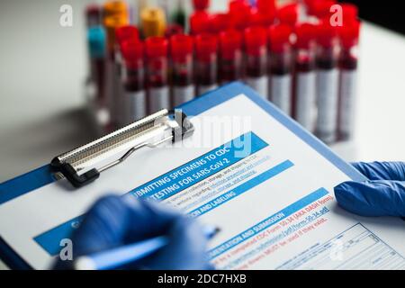 Un technicien de laboratoire remplit le formulaire de soumission d'échantillon, test de laboratoire pour le COV-SRAS-2 nouvelle maladie du virus corona, gros plan des mains dans des gants tenant Banque D'Images