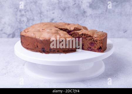 Tarte au chocolat avec cerises sur un support à gâteau blanc, un morceau coupé. Cuisson maison. Gros plan. Banque D'Images