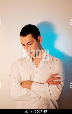 Jeune homme, croisant les bras, regardant vers le bas. Banque D'Images