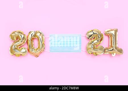 Ballons en aluminium sous la forme de numéros 2021 avec masque de protection sur fond rose, vue de dessus. Nouveau concept de célébration normale du nouvel an. Banque D'Images