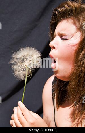 Une jeune femme, une adolescente, soufflant les graines d'une fleur de pissenlit à la fin de l'été. Banque D'Images