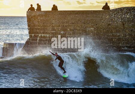 Brighton Royaume-Uni 19 novembre 2020 - UN surfeur attrape une vague au coucher du soleil au large de Brighton Beach tandis que les gens apprécient la fin de la journée le long de la côte sud : Credit Simon Dack / Alay Live News Banque D'Images