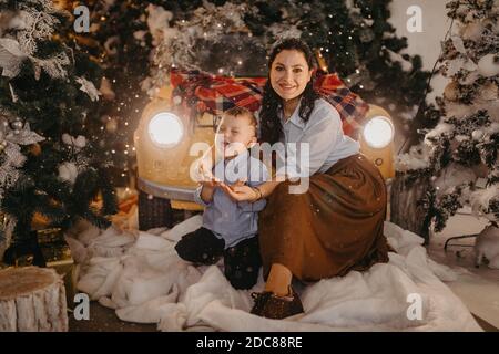 Mère et fils ont un plaisir près de voiture rétro et arbre de Noël avec des décorations sur fond de flocons de neige tombant. Banque D'Images