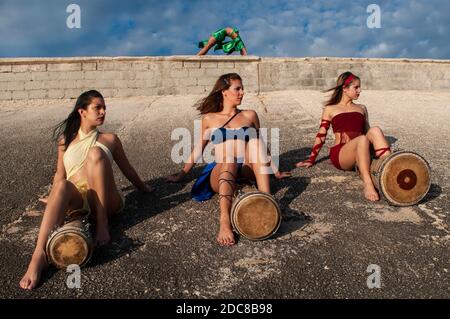 Quatre filles vêtues de couleurs différentes avec leur visage peint poser avec des tambours assis sur une colline de pierre Banque D'Images