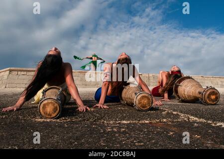 Quatre filles vêtues de couleurs différentes avec leur visage peint pose avec des tambours assis sur leur dos sur un rocailleux côte Banque D'Images