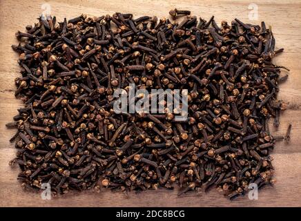 Vue de dessus de la pile de clous de girofle séchés aromatiques éparpillés forme rectangulaire sur table en bois Banque D'Images