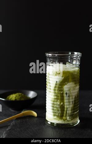 Latte glacée au matcha vert dans un long verre sur fond noir. La vie encore du thé matcha. Banque D'Images