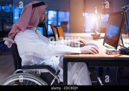 Homme d'affaires arabe handicapé dans la tradition suit travaillant en fonction pendant la pandémie de coronavirus. Homme d'affaires handicapé dans le fauteuil roulant travaille en ligne i Banque D'Images