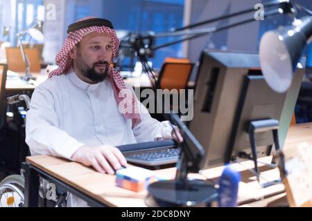 Homme d'affaires arabe handicapé dans la tradition suit travaillant en fonction pendant la pandémie de coronavirus. Homme d'affaires handicapé dans le fauteuil roulant travaille en ligne i Banque D'Images