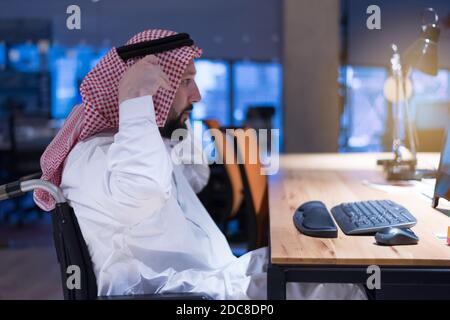 Homme d'affaires arabe handicapé dans la tradition suit travaillant en fonction pendant la pandémie de coronavirus. Homme d'affaires handicapé dans le fauteuil roulant travaille en ligne i Banque D'Images