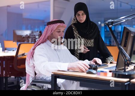 Un homme d'affaires arabe handicapé dans la tradition s'adapte avec une femme arabe assiposante travaillant au bureau. Homme d'affaires handicapés dans le fauteuil roulant travaille dans l'o Banque D'Images
