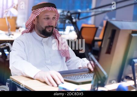 Homme d'affaires arabe handicapé dans la tradition suit travaillant en fonction pendant la pandémie de coronavirus. Homme d'affaires handicapé dans le fauteuil roulant travaille en ligne i Banque D'Images