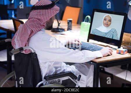 Homme d'affaires arabe handicapé dans la tradition suit travaillant en fonction pendant la pandémie de coronavirus. Homme d'affaires handicapé dans le fauteuil roulant travaille en ligne i Banque D'Images