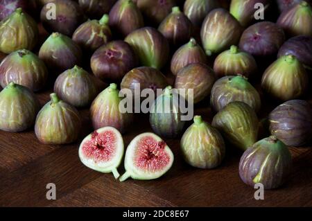 Une figue fraîchement cueillie “Ficus carica” coupée en deux pour révéler les graines et la chair rouge succulente. Sur fond de figues disposées sur une table en bois. Banque D'Images