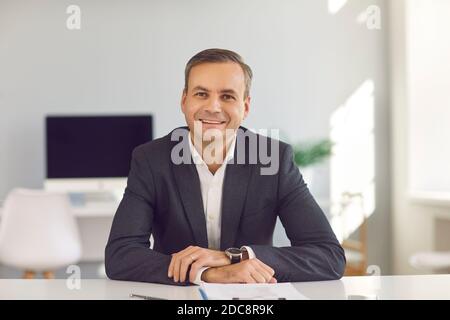 Jeune homme d'affaires souriant assis et regardant l'appareil photo en ligne vidéo au bureau Banque D'Images