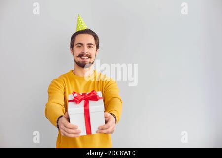 Jeune homme souriant dans un chapeau de clown festif montrant un cadeau de vacances pendant la vidéo Banque D'Images