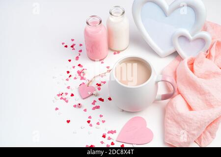 Fond pour février 14 avec une tasse de café avec du lait, un cadre en forme de coeur et une bouteille de lait sur fond blanc avec des coeurs. Banque D'Images