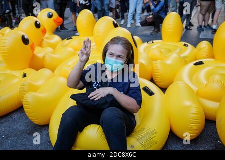 Un manifestant se fait un hommage aux trois doigts tout en étant assis sur un canard jaune gonflable pendant la manifestation.des milliers de manifestants pro-démocratie se sont rassemblés à l'intersection de Ratchaprasong pour asperger et pulvériser de la peinture au siège de la police royale thaïlandaise demandant un changement constitutionnel par le gouvernement. Banque D'Images