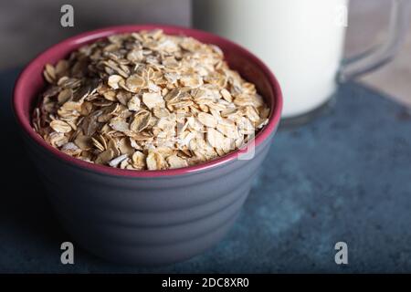 Séchez les flocons d'avoine dans un bol avec du lait sur fond bleu foncé. Des flocons de céréales sains dans un bol en céramique et un verre de lait en gros plan. Banque D'Images