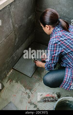 Femme ouvrier posant un nouveau plancher de carrelage Banque D'Images