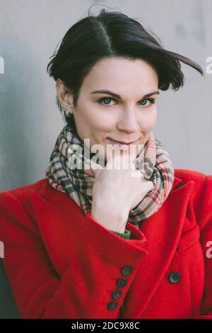 Female dressed in a warm coat smiles at the camera - Scarf - Winter - Seasonal Stock Photo