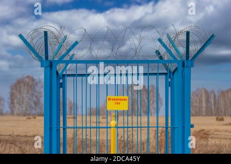 Photo d'une station de gaz industriel en cage avec barbelés sur le dessus de la clôture. Tuyau de gaz jaune au milieu de la cage. La plaque jaune sur la clôture indique i Banque D'Images