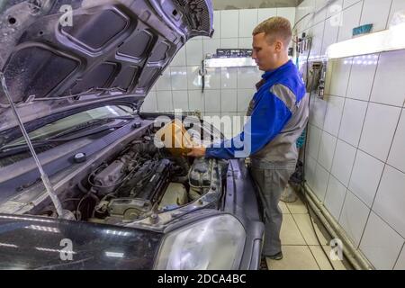Le mécanicien de voiture remplace et verse de l'huile dans le moteur à la station-service pendant la routine de vérification régulière. Banque D'Images