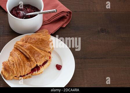 Croissant rempli de confiture sur une assiette, avec une casserole de conservation. Placé sur une table en bois. Banque D'Images
