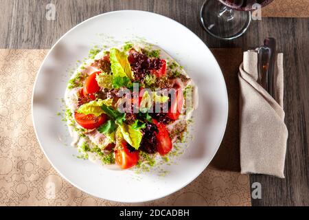 Salade verte avec tomate et jambon fumé. Verre de vin rouge en arrière-plan. Vue du dessus. Lumière de la fenêtre du restaurant Banque D'Images