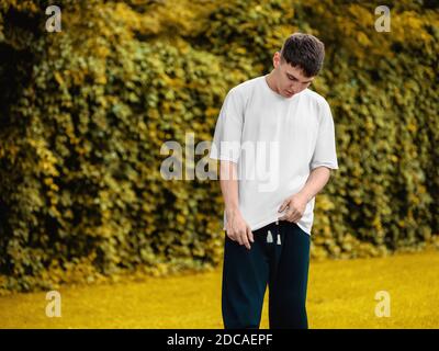 Maquette de t-shirt blanc sur un jeune homme avec sa tête vers le bas, debout sur un fond flou d'automne dans le parc, vêtements vierges pour la présentation de design, p Banque D'Images