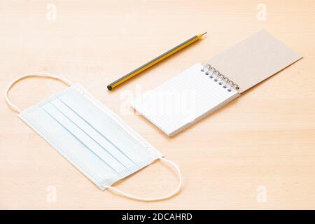 Un masque facial et un bloc-notes en spirale vierge avec un stylo sont disposés sur une table en bois. Concept de liste à faire pendant l'épidémie de Covid-19. Banque D'Images