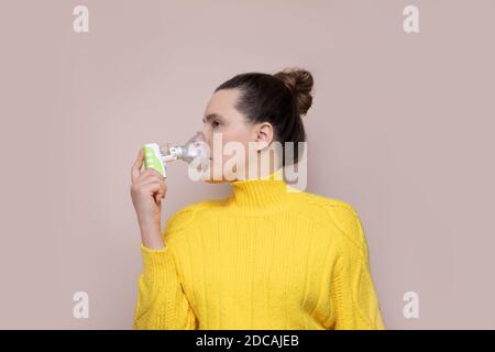 Une femme de 40 ans dans un chandail jaune sur fond rose inhale les voies respiratoires supérieures, les poumons avec un nébuliseur. Vue sur l'extérieur. Photo de studio Banque D'Images