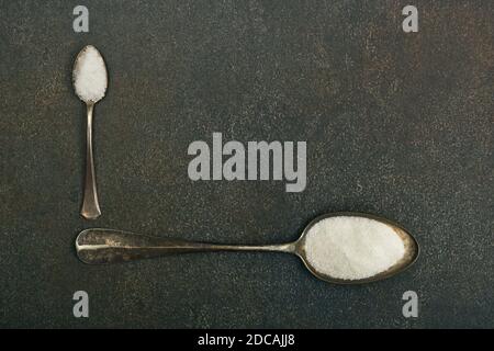 Gros plan à plat posez deux cuillères en métal vintage de sucre blanc et de sel de mer sur la surface de la table en pierre de grunge sombre avec espace de copie, vue du dessus en hauteur, directement Banque D'Images
