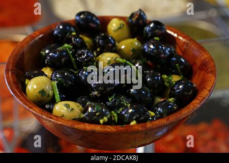 Gros plan traditionnel artisanal mariné olives noires et vertes avec des herbes d'épices dans le bol rustique en bois naturel sur la présentation au détail de marché ouvert, haut an Banque D'Images